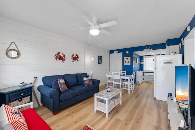 living room with ceiling fan, wood walls, and light wood-type flooring