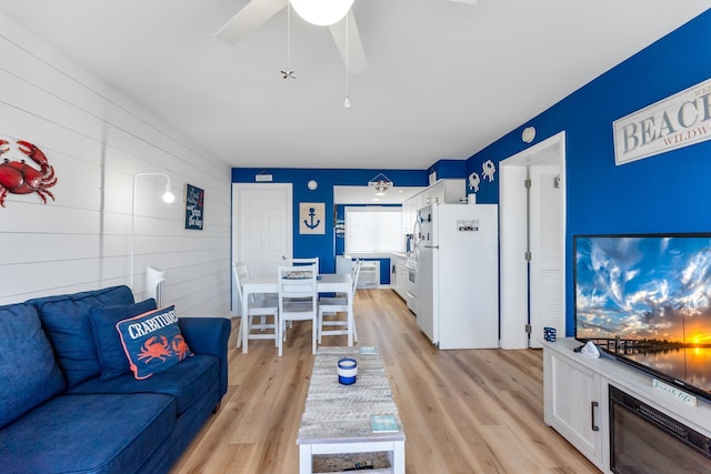 living room featuring light hardwood / wood-style floors, ceiling fan, and wood walls