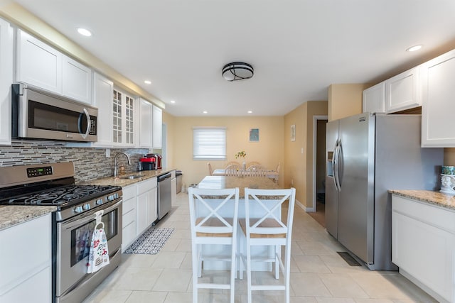 kitchen with sink, light stone counters, white cabinetry, appliances with stainless steel finishes, and decorative backsplash