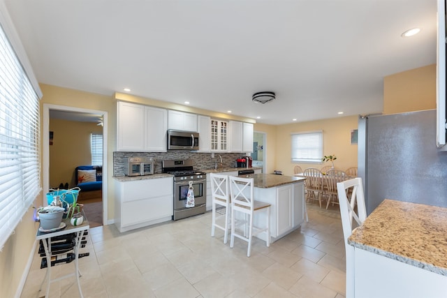 kitchen featuring stainless steel appliances, tasteful backsplash, light stone countertops, white cabinets, and a kitchen island