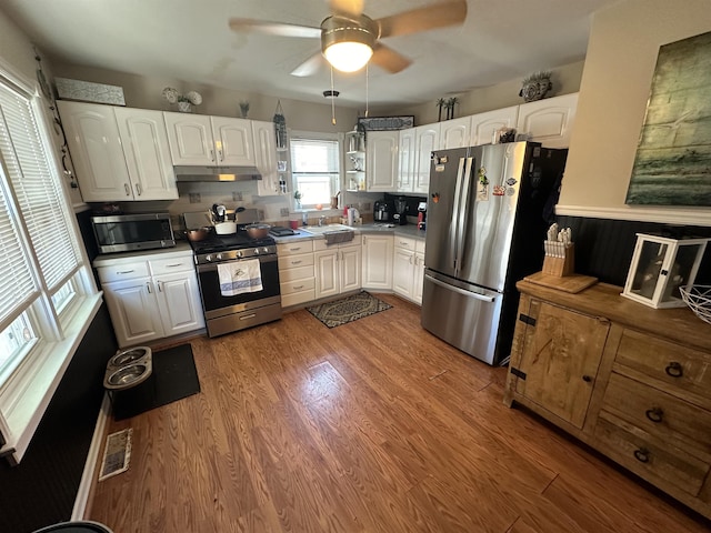 kitchen with appliances with stainless steel finishes, white cabinetry, and hardwood / wood-style floors