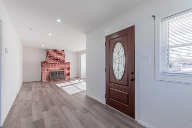 foyer entrance featuring plenty of natural light, a brick fireplace, and light hardwood / wood-style flooring