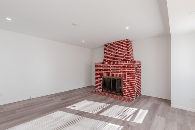 unfurnished living room with light wood-type flooring and a brick fireplace