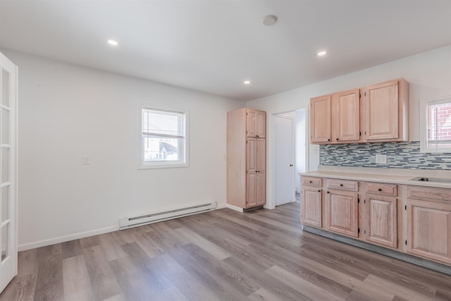 kitchen with tasteful backsplash, light brown cabinetry, a baseboard heating unit, and light wood-type flooring