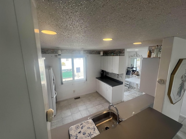 kitchen featuring a sink, freestanding refrigerator, dark countertops, white cabinetry, and a textured ceiling