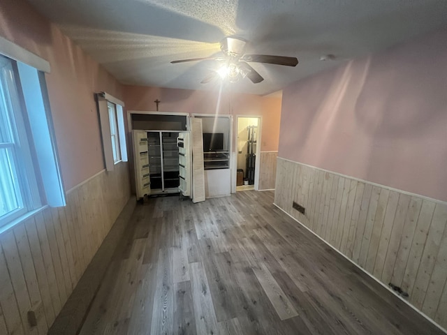 unfurnished living room with a wainscoted wall, ceiling fan, wood walls, healthy amount of natural light, and wood finished floors