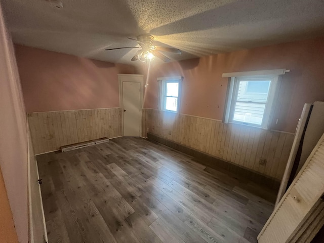 unfurnished room featuring wainscoting, wood walls, a textured ceiling, a ceiling fan, and wood finished floors