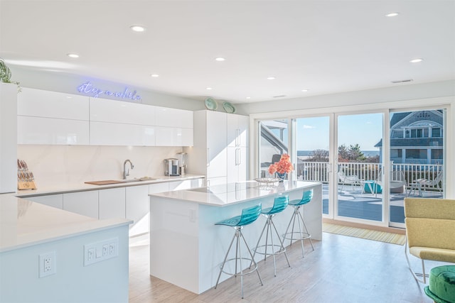 kitchen featuring sink, a kitchen island, a breakfast bar area, white cabinets, and light wood-type flooring