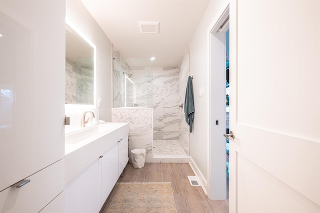 bathroom featuring a tile shower, vanity, and wood-type flooring