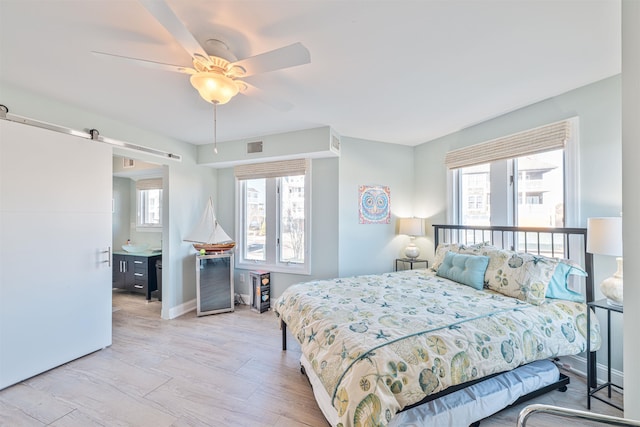 bedroom with multiple windows, a barn door, light hardwood / wood-style flooring, and ceiling fan