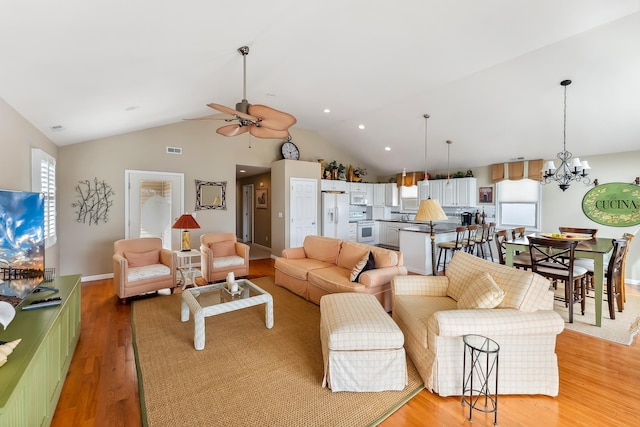 living room featuring visible vents, baseboards, lofted ceiling, light wood-style flooring, and ceiling fan with notable chandelier