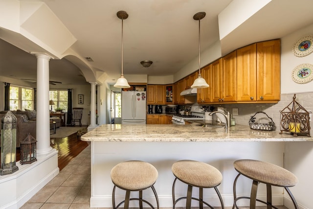 kitchen with white refrigerator, kitchen peninsula, gas stove, and ornate columns