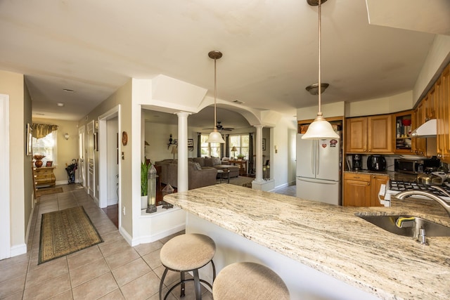 kitchen featuring ornate columns, decorative light fixtures, a breakfast bar area, white fridge, and kitchen peninsula