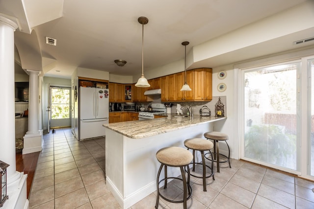 kitchen featuring white appliances, decorative light fixtures, kitchen peninsula, and decorative columns