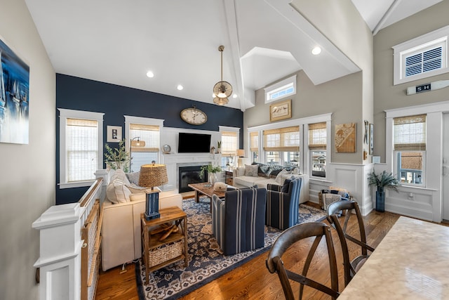 243 110th St, Stone Harbor, NJ 08247 - living room featuring wood finished floors, a glass covered fireplace, high vaulted ceiling, a wainscoted wall, and recessed lighting