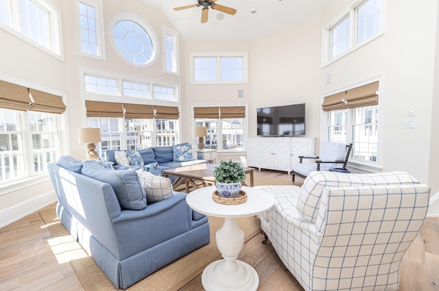 living room with ceiling fan, a towering ceiling, light hardwood / wood-style floors, and a healthy amount of sunlight