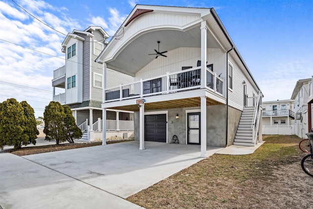 coastal home featuring a garage, driveway, stairs, and a ceiling fan