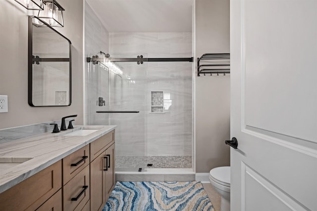 bathroom featuring double vanity, toilet, a stall shower, a sink, and baseboards