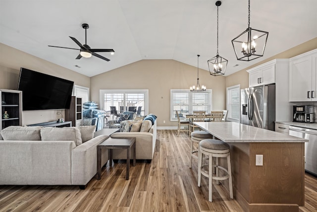 living room with light wood-style floors, baseboards, vaulted ceiling, and ceiling fan with notable chandelier