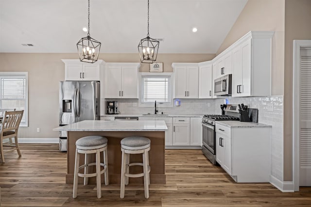 kitchen with stainless steel appliances, a sink, visible vents, vaulted ceiling, and a center island