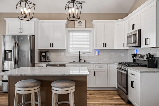 kitchen featuring a breakfast bar, light wood finished floors, stainless steel appliances, white cabinetry, and a sink