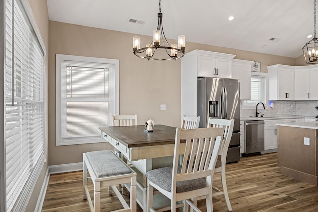 dining space with baseboards, visible vents, wood finished floors, vaulted ceiling, and a chandelier