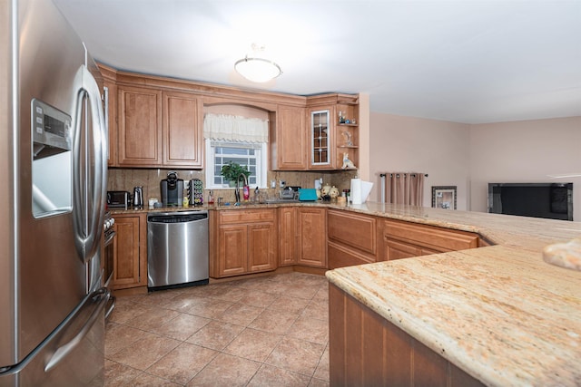 kitchen with decorative backsplash, appliances with stainless steel finishes, kitchen peninsula, light stone counters, and sink