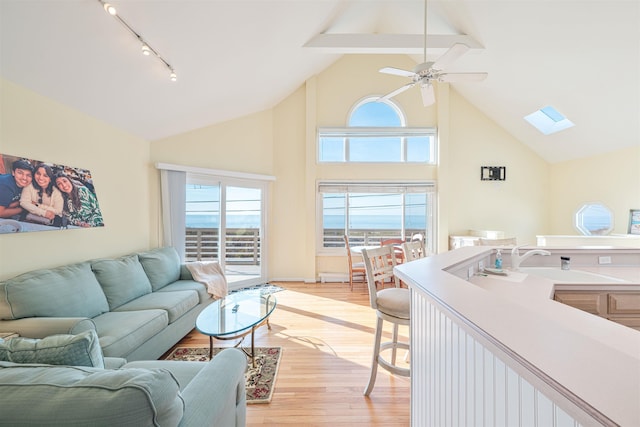 living room featuring light wood-type flooring, a skylight, ceiling fan, sink, and beam ceiling