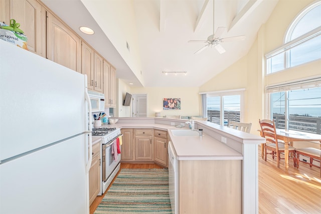 kitchen with kitchen peninsula, light brown cabinetry, white appliances, sink, and high vaulted ceiling