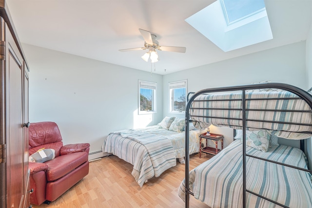 bedroom with a baseboard heating unit, a skylight, ceiling fan, light wood-type flooring, and a closet