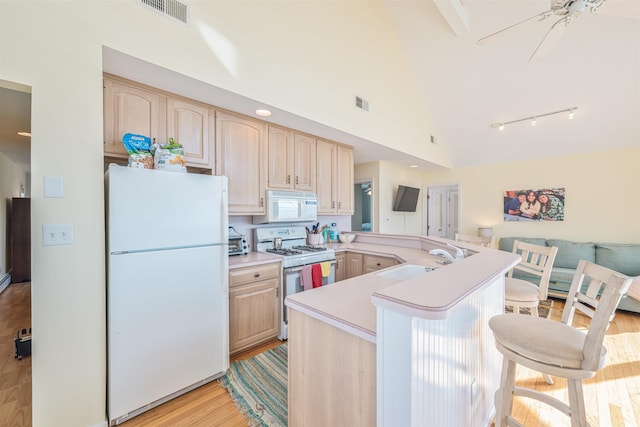 kitchen featuring light brown cabinets, white appliances, sink, a kitchen bar, and kitchen peninsula