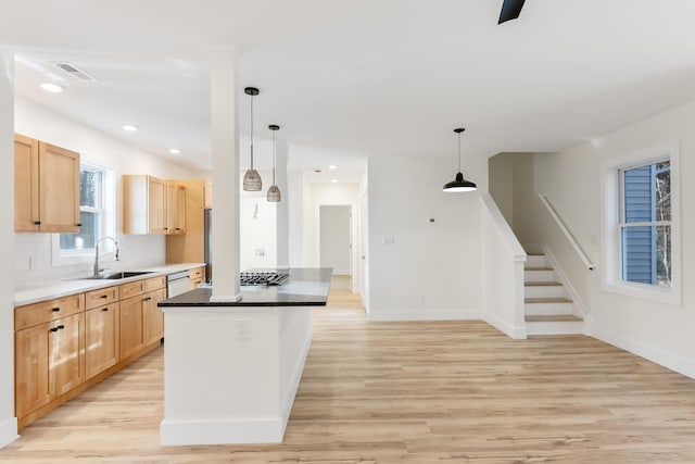 kitchen with light brown cabinetry, sink, hanging light fixtures, and light wood-type flooring