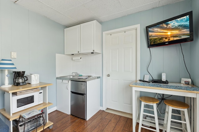 kitchen with refrigerator, a drop ceiling, dark wood-type flooring, white cabinetry, and a breakfast bar area