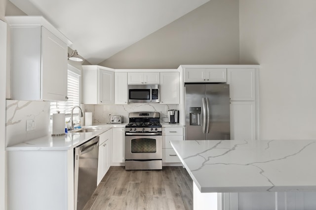 kitchen featuring decorative backsplash, white cabinets, stainless steel appliances, and light stone counters