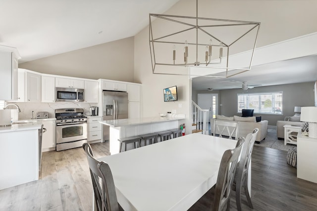 dining space featuring ceiling fan, sink, high vaulted ceiling, and light hardwood / wood-style flooring