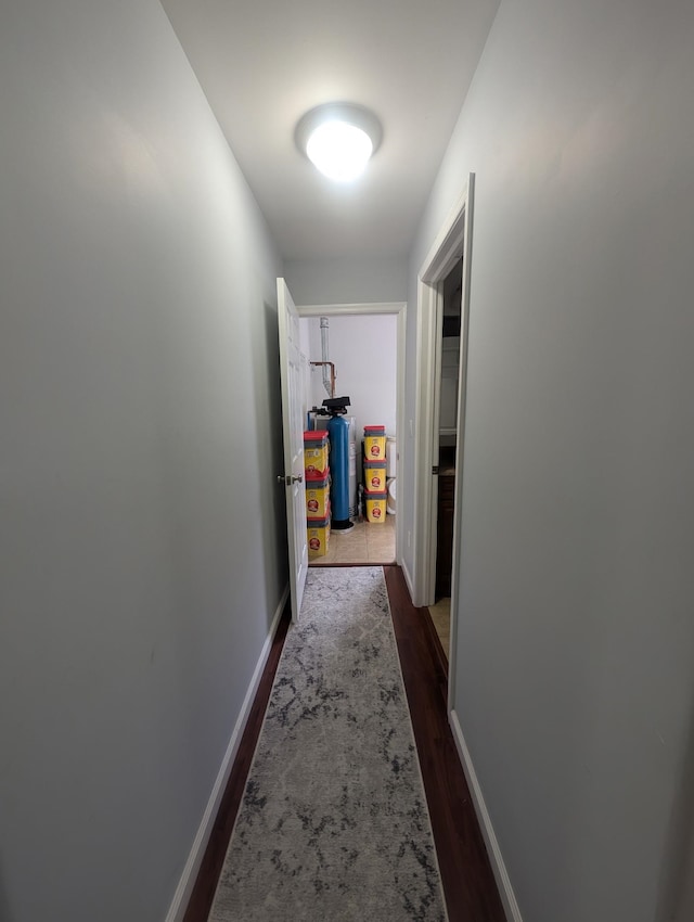 hall featuring baseboards, water heater, and dark wood-style flooring