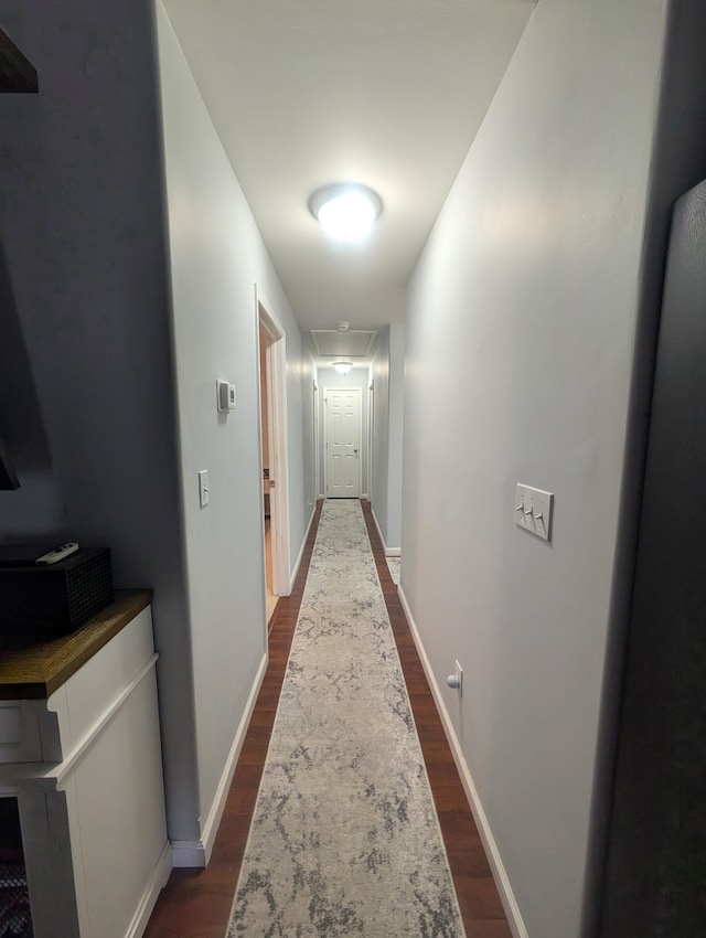 hall with attic access, baseboards, and dark wood-style floors