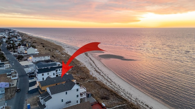 aerial view at dusk featuring a water view and a view of the beach