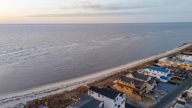 aerial view at dusk featuring a water view and a beach view