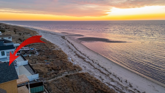 aerial view at dusk featuring a water view and a view of the beach