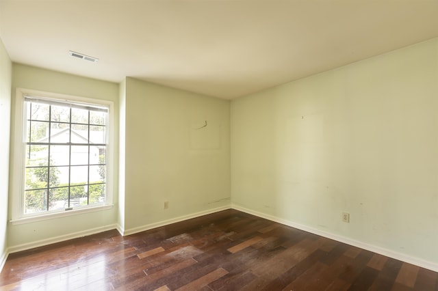 empty room featuring dark wood-type flooring, visible vents, and baseboards