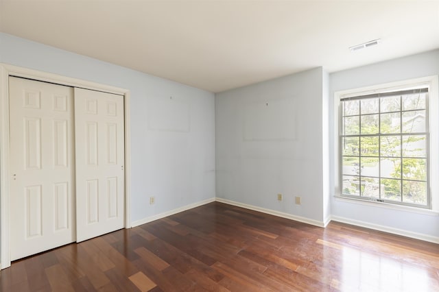 unfurnished bedroom with baseboards, wood finished floors, visible vents, and a closet