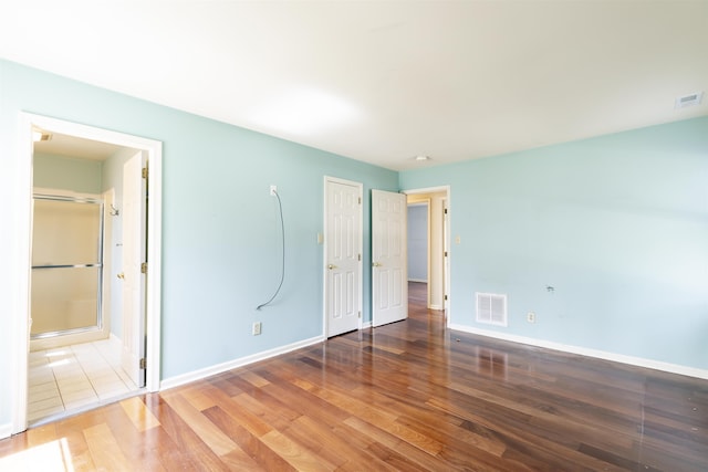 unfurnished bedroom featuring wood finished floors, visible vents, baseboards, and ensuite bathroom