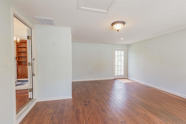 unfurnished room with attic access, wood finished floors, visible vents, and baseboards