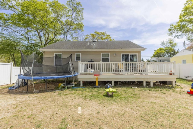 back of property featuring a yard, fence, a wooden deck, and a trampoline