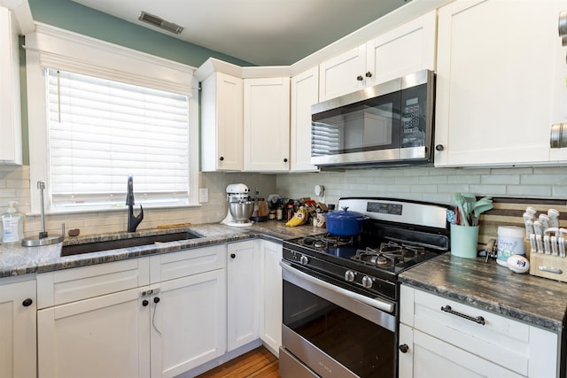 kitchen with backsplash, visible vents, a sink, stainless steel appliances, and white cabinetry