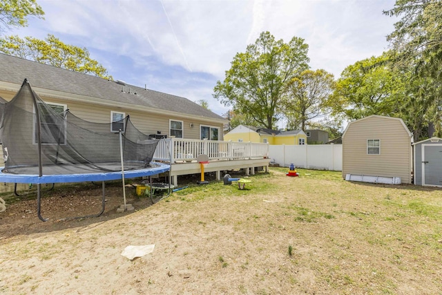 view of yard with fence, a trampoline, a storage shed, a wooden deck, and an outbuilding