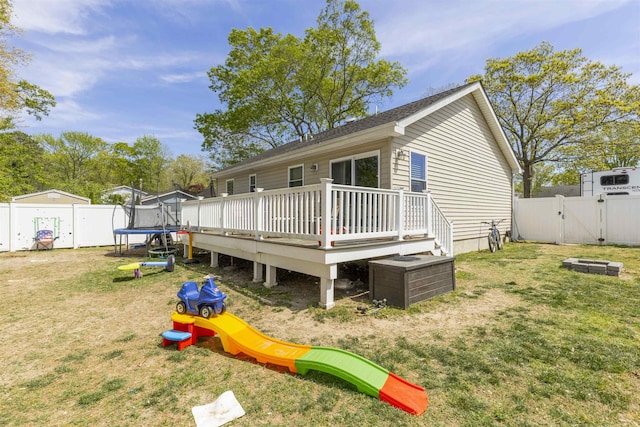 back of house featuring a trampoline, a lawn, a wooden deck, a gate, and a fenced backyard