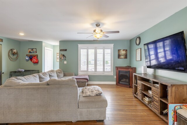 living room with ceiling fan, light wood finished floors, a glass covered fireplace, recessed lighting, and baseboards