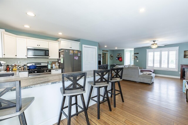 kitchen featuring a kitchen breakfast bar, decorative backsplash, appliances with stainless steel finishes, recessed lighting, and white cabinetry